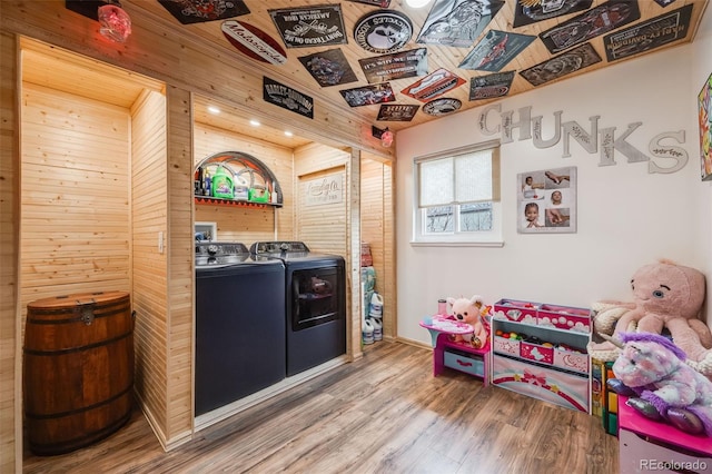 game room with wood-type flooring, washing machine and dryer, and wood walls