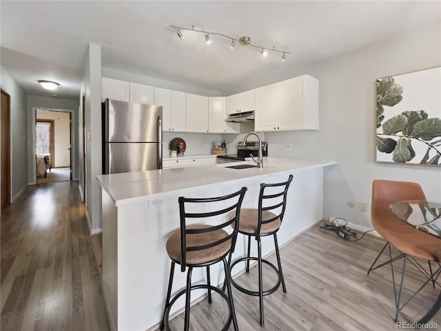 kitchen featuring light countertops, appliances with stainless steel finishes, a sink, a peninsula, and under cabinet range hood