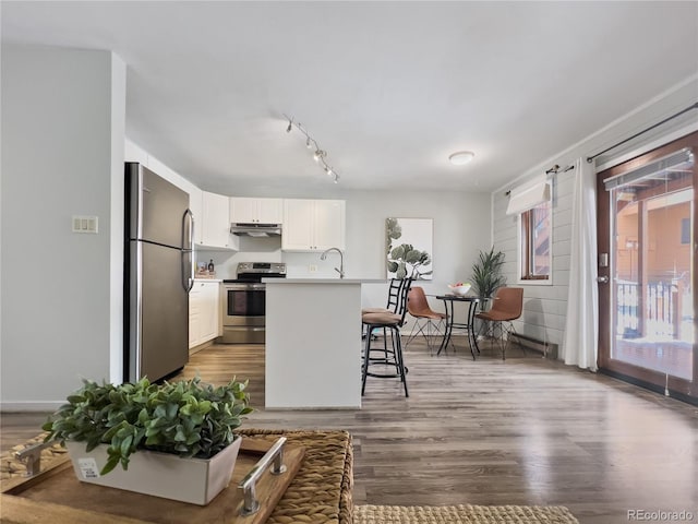 kitchen with a breakfast bar, dark wood finished floors, stainless steel appliances, white cabinetry, and under cabinet range hood