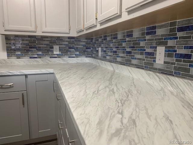 interior details featuring decorative backsplash, light stone countertops, and gray cabinetry