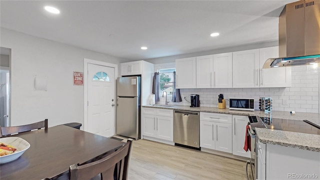 kitchen featuring light wood-type flooring, wall chimney exhaust hood, stainless steel appliances, sink, and white cabinetry