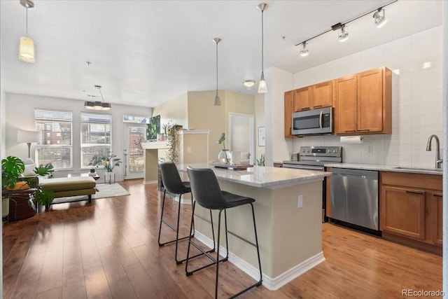 kitchen featuring appliances with stainless steel finishes, a center island, a breakfast bar, sink, and decorative light fixtures