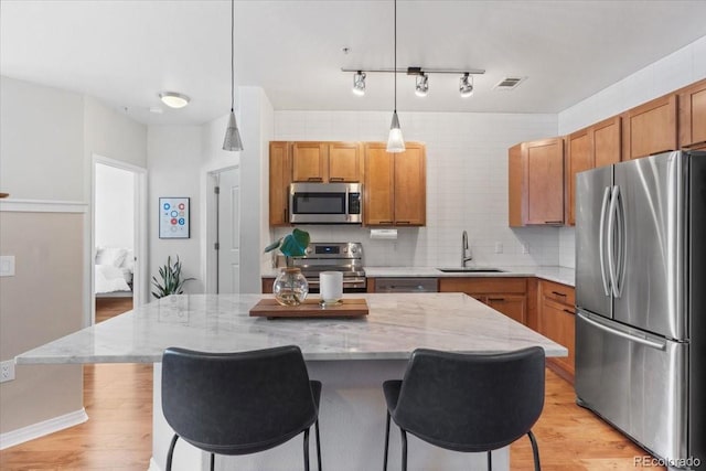 kitchen featuring stainless steel appliances, sink, decorative light fixtures, a center island, and light stone counters