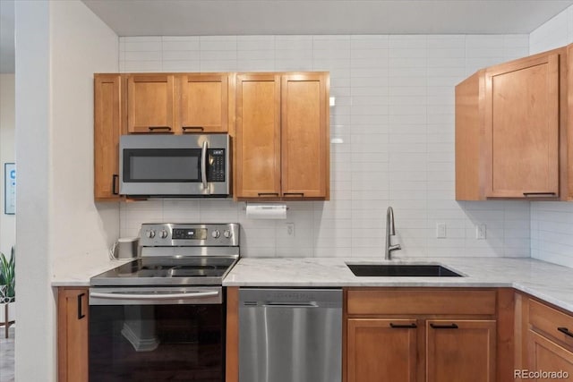 kitchen with light stone countertops, appliances with stainless steel finishes, decorative backsplash, and sink