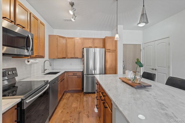 kitchen with light stone countertops, hanging light fixtures, stainless steel appliances, tasteful backsplash, and sink