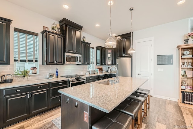 kitchen with light hardwood / wood-style flooring, sink, light stone counters, an island with sink, and stainless steel appliances