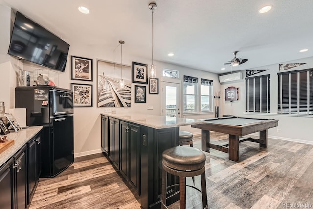 kitchen featuring light stone countertops, pendant lighting, black refrigerator, a kitchen breakfast bar, and hardwood / wood-style flooring