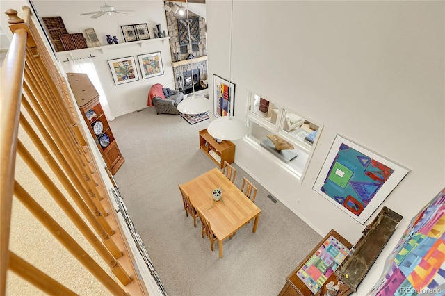 living area featuring carpet floors, a stone fireplace, a towering ceiling, and ceiling fan