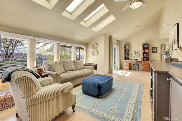 living area featuring high vaulted ceiling, a ceiling fan, light wood finished floors, and a skylight
