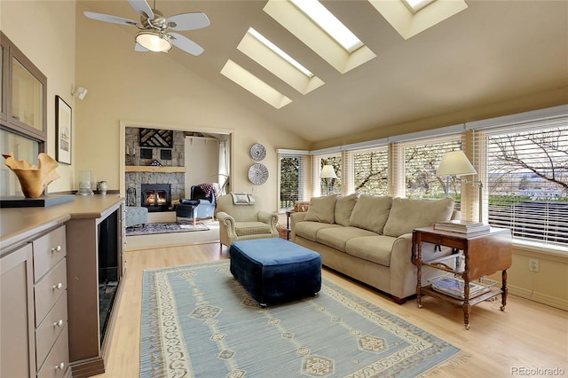 living area featuring high vaulted ceiling, a ceiling fan, a skylight, light wood-type flooring, and a fireplace