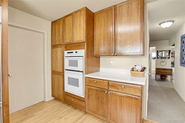 kitchen featuring light wood-type flooring, light countertops, brown cabinets, and double oven