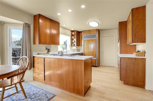 kitchen with light wood finished floors, light countertops, open shelves, a peninsula, and brown cabinetry