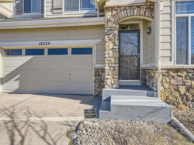 entrance to property featuring an attached garage, stone siding, and concrete driveway