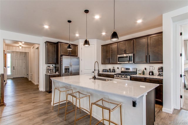 kitchen with appliances with stainless steel finishes, a sink, dark brown cabinetry, a kitchen bar, and recessed lighting