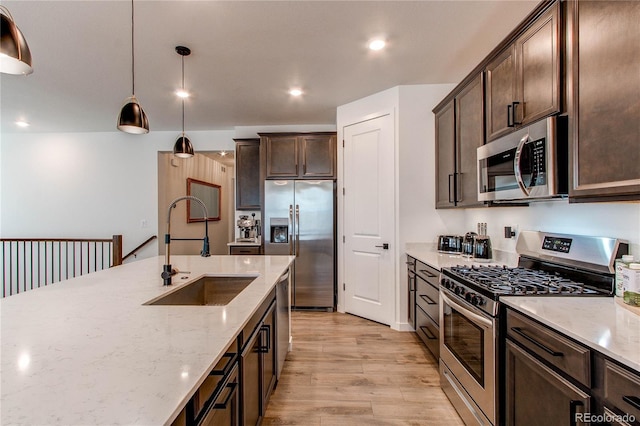 kitchen featuring appliances with stainless steel finishes, a sink, light wood finished floors, dark brown cabinetry, and light stone countertops