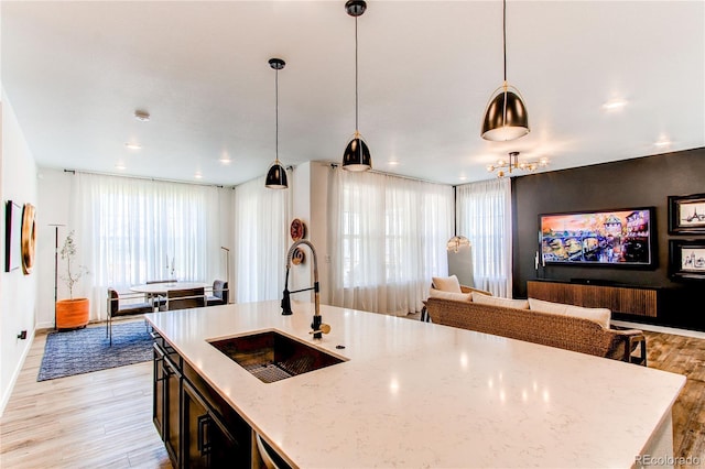kitchen with a sink, light wood finished floors, open floor plan, light stone counters, and decorative light fixtures