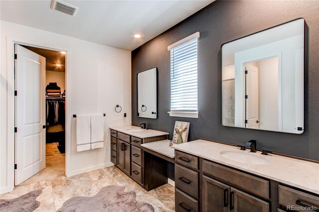 bathroom featuring two vanities, a walk in closet, marble look tiles, recessed lighting, and baseboards
