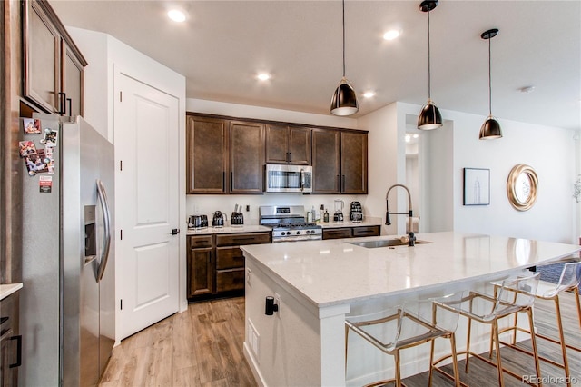 kitchen featuring stainless steel appliances, a sink, light wood-style flooring, light stone countertops, and a kitchen island with sink