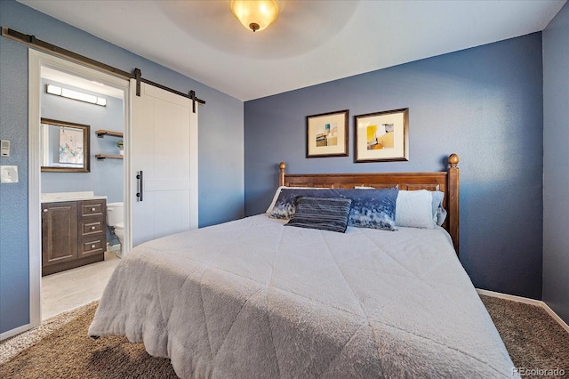 carpeted bedroom with a barn door, ceiling fan, and ensuite bath