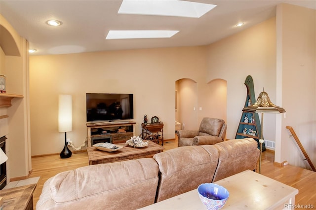 living room featuring a skylight, baseboards, arched walkways, light wood-type flooring, and recessed lighting