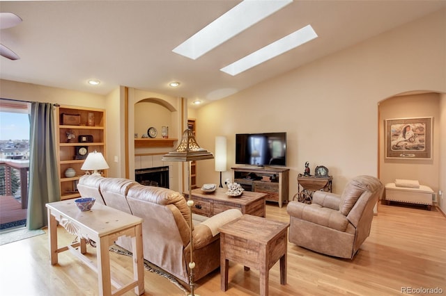 living area featuring recessed lighting, light wood-style floors, vaulted ceiling with skylight, and a tile fireplace