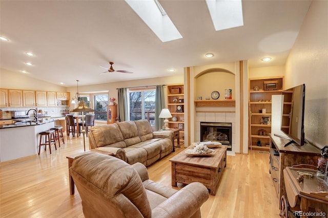 living room featuring vaulted ceiling with skylight, a fireplace, light wood finished floors, and recessed lighting