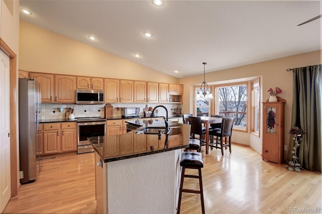 kitchen featuring decorative backsplash, lofted ceiling, appliances with stainless steel finishes, a breakfast bar, and a sink