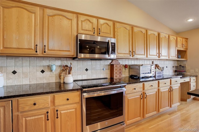 kitchen with tasteful backsplash, lofted ceiling, light wood-style flooring, appliances with stainless steel finishes, and dark stone countertops