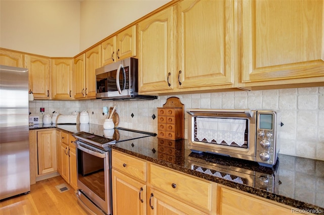 kitchen featuring dark stone counters, stainless steel appliances, backsplash, and light brown cabinets