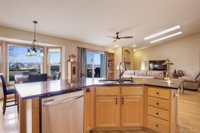 kitchen with a sink, open floor plan, stainless steel dishwasher, dark stone counters, and a center island with sink