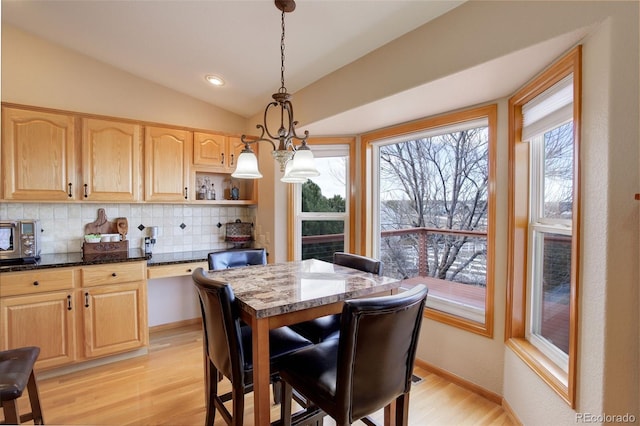 dining area with vaulted ceiling, light wood-type flooring, baseboards, and a healthy amount of sunlight