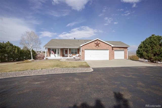 ranch-style home featuring brick siding, a porch, a garage, driveway, and a front lawn