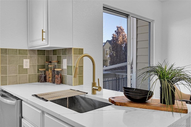 kitchen featuring decorative backsplash, light stone counters, sink, dishwasher, and white cabinetry