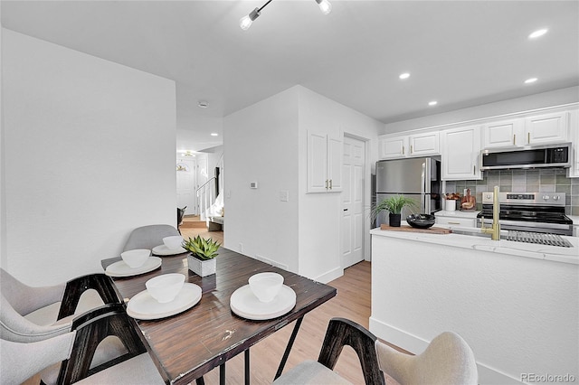 kitchen with appliances with stainless steel finishes, backsplash, light hardwood / wood-style flooring, and white cabinetry