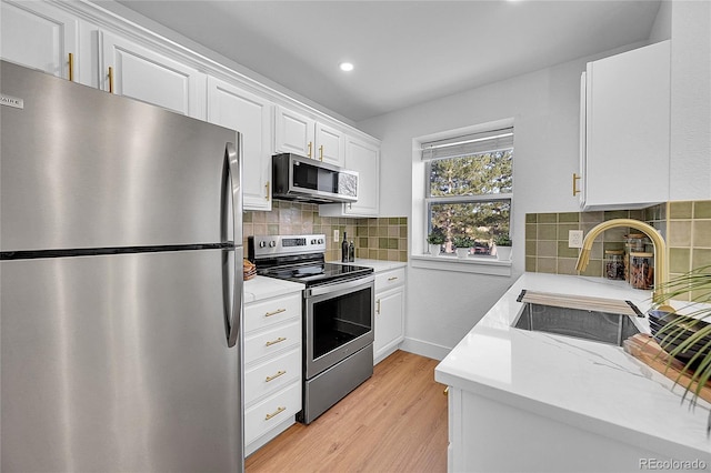 kitchen with appliances with stainless steel finishes, tasteful backsplash, sink, light hardwood / wood-style floors, and white cabinetry