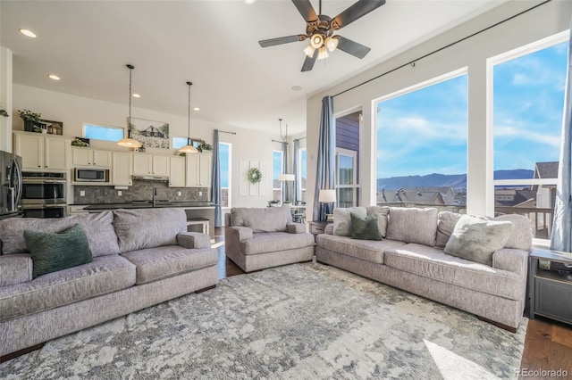 living room with a mountain view, dark wood-type flooring, ceiling fan, and a healthy amount of sunlight