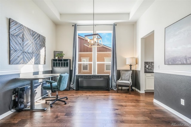 office area with a raised ceiling, dark wood-type flooring, and an inviting chandelier