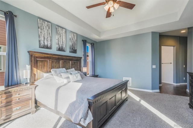 bedroom with dark colored carpet, ceiling fan, and a tray ceiling