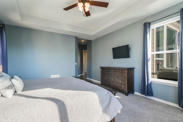 carpeted bedroom featuring a raised ceiling and ceiling fan