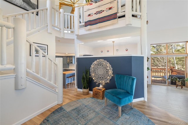 living area featuring stairway, baseboards, a towering ceiling, and wood finished floors