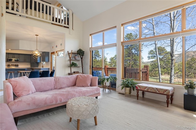 living area featuring light wood finished floors, plenty of natural light, high vaulted ceiling, and a chandelier