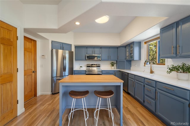 kitchen with a kitchen breakfast bar, a sink, blue cabinets, stainless steel appliances, and light wood finished floors