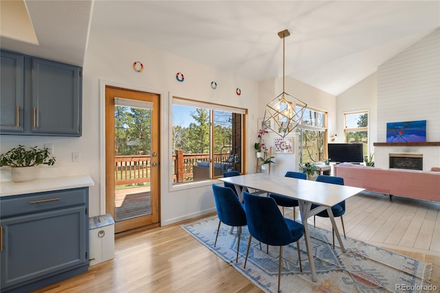 dining area with a wealth of natural light, lofted ceiling, a brick fireplace, and light wood-style floors