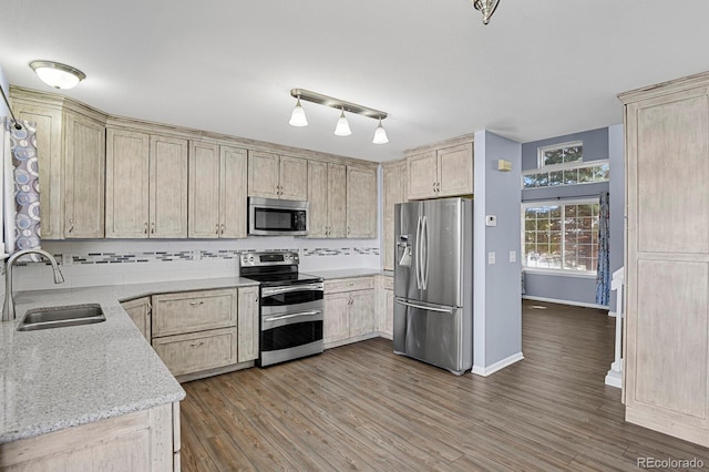 kitchen featuring wood finished floors, decorative backsplash, appliances with stainless steel finishes, a sink, and light stone countertops