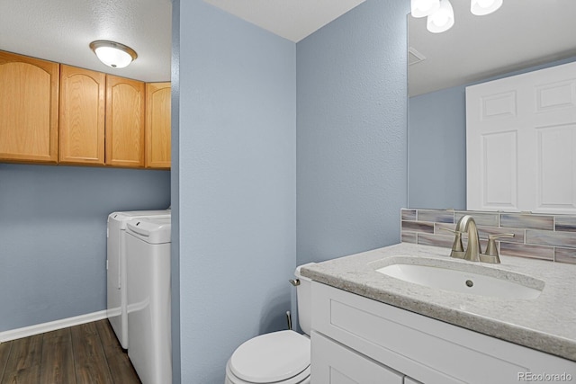 half bathroom with toilet, separate washer and dryer, wood finished floors, vanity, and baseboards