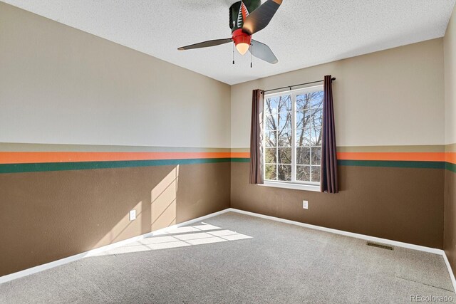 carpeted spare room featuring baseboards, ceiling fan, visible vents, and a textured ceiling