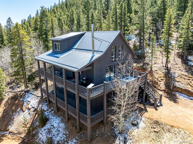 back of property with stairs, metal roof, a deck, and a forest view