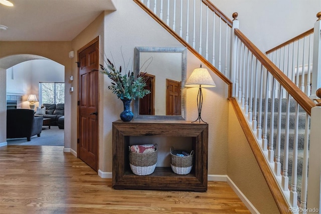 hallway with arched walkways, baseboards, light wood finished floors, and stairs