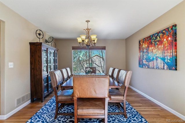 dining area featuring baseboards, light wood-type flooring, visible vents, and an inviting chandelier