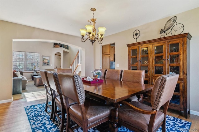 dining space with light wood finished floors, baseboards, arched walkways, stairs, and a chandelier